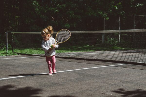 Young girl holding a tennis racket and ball on a tennis court. Her parents have just read how to begin Nurturing Children with Love: Key Principles for Gentle Discipline