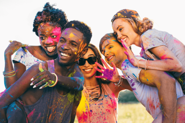 Diverse group of young friends laughing and covered in colorful powder, symbolizing connection and joy.