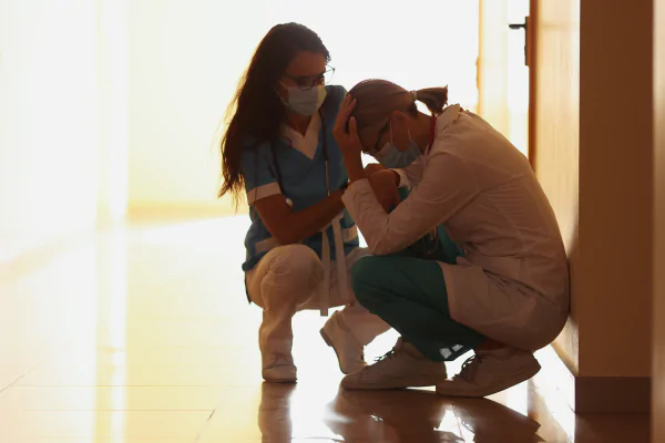 A nurse recommending Christian Counseling and supporting a distressed healthcare worker sitting on the floor, symbolizing the importance of mental health and preventing burnout in high-stress professions.