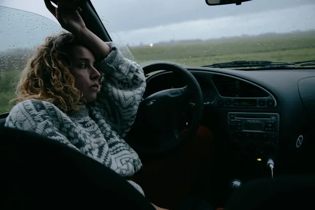 A thoughtful woman sitting in a parked car on a rainy day, gazing out the window, symbolizing introspection and overthinking.